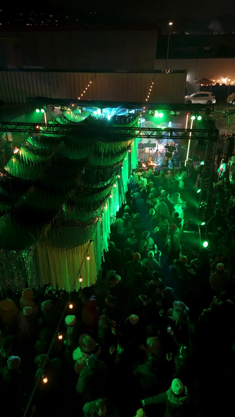 The teal tinsel canopy over a packed yard, straight down from the drone