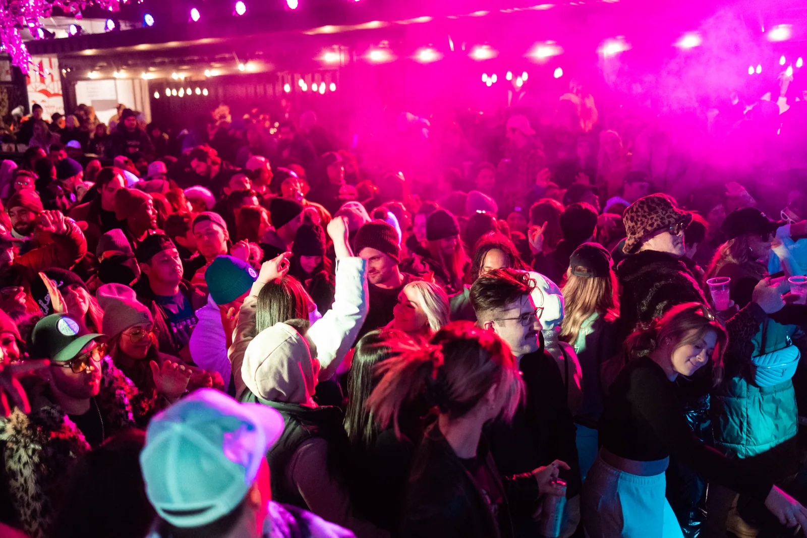 A packed dance floor in pink smoke, hands up